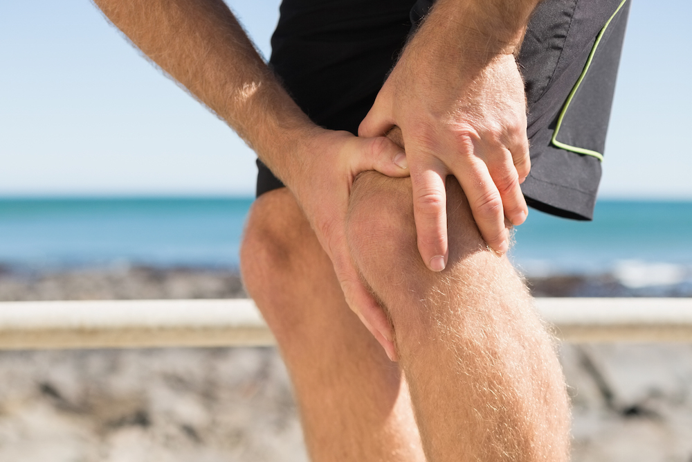 Fit man gripping his injured knee on a sunny day